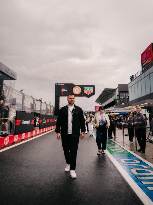 A man walks down a wet pit lane at the Zandvoort circuit beneath a TAG Heuer and Fanatec branded gantry, with Formula 1 signage visible along the barrier. The scene captures the backdrop of the post's message about tech's growing presence on the F1 grid, with Crypto.com and other sponsor branding visible throughout the paddock.