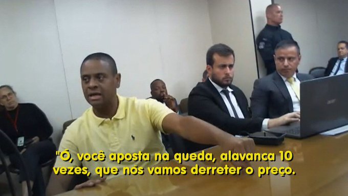 A man identified as "Bitcoin Pharaoh" speaks at what appears to be a court proceeding, accompanied by suited lawyers, with Portuguese subtitles reading "'O, você aposta na queda, alavanca 10 vezes, que nós vamos derreter o preço'" (translating to "Oh, you bet on the drop, 10x leverage, that we will melt the price"), reflecting his role in a cryptocurrency fraud case involving R$ 7 million seized by Federal Police.