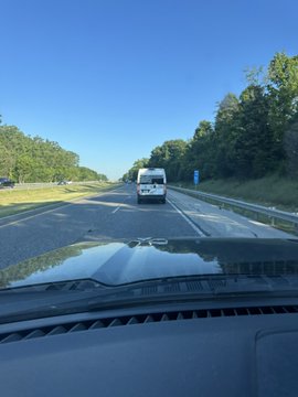 A highway scene captured from inside a vehicle shows a white recreational vehicle (RV) driving ahead on a clear, sunny day. The image playfully relates to the post's theme about unconventional payment methods on the road, humorously suggesting the RV's rear would be the perfect spot to display a Bitcoin address for travelers to send crypto tips.