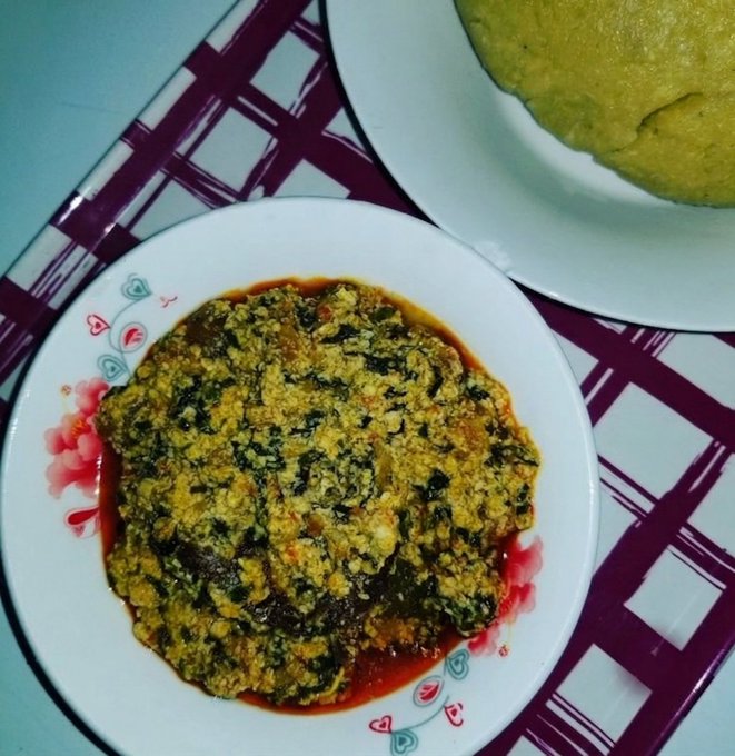 A plate of egusi soup (melon seed stew with greens) served alongside a portion of yellow eba (garri) on a patterned tray, representing a traditional Nigerian meal that the poster enjoyed for $300.