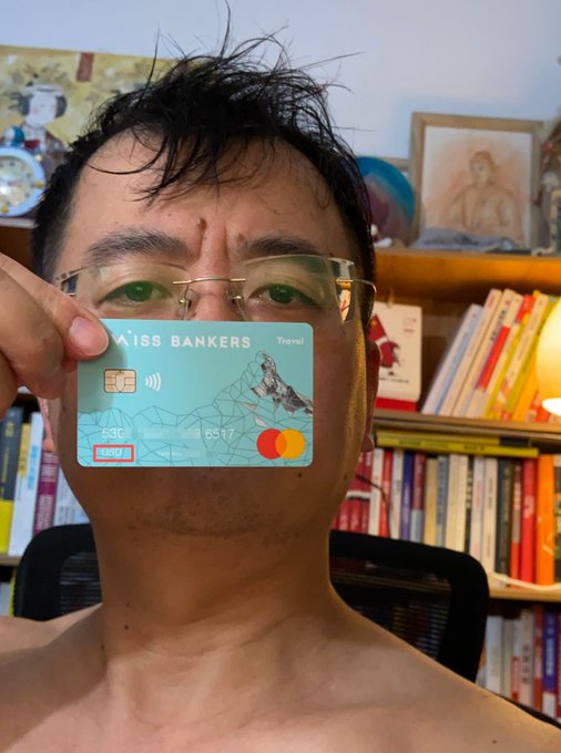 A shirtless man holds up a teal "Swiss Bankers Travel" Mastercard (ending in 9651) featuring a mountain design, likely showcasing the card mentioned in his post about overseas debit card options.