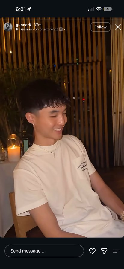 A young man with dark hair and an earring smiles while seated at a dimly lit outdoor table, shown in an Instagram story screenshot from user 'gunna' posted '37m' ago with text 'Gunna · bn one tonight'.