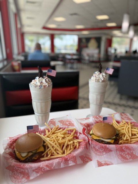 Two cheeseburgers with fries and vanilla milkshakes topped with American flags served at a classic American diner.