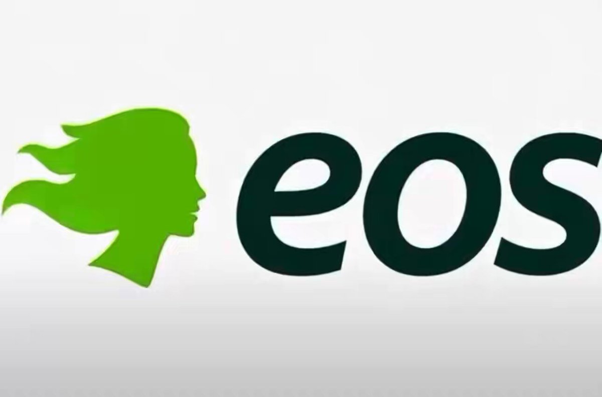 The image features a logo for EOS Energy Storage Systems, which is a partnership between EOS Energy and Frontier Power USA. The logo consists of an illustration of a woman's face with green hair against a white background. Below the woman's head, there are two words written in black text that read "EOS". This logo represents the company's commitment to developing long-term energy storage solutions for renewable power sources like solar and wind power. It also highlights EOS Energy Systems' partnership with Frontier Power USA to expand their existing 2+ GWh battery storage projects into Eos Z3 systems, which can help fulfill Frontier Energy's deployment agreements.