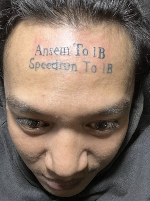 A close-up photo shows a man's forehead freshly tattooed with the text "Ansem To 1B" and "Speedrun To 1B," capturing the viral moment when crypto user "ghniy_" permanently inked his support for the $ANSEM token ("The Black Bull") and his belief that it can reach a $1 billion market cap.