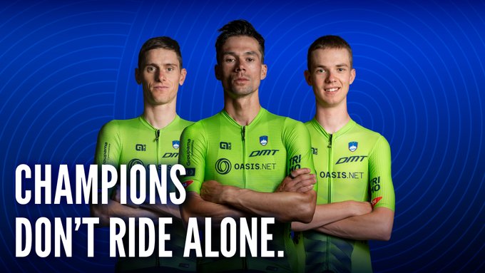 The image shows three male cyclists in matching green and yellow jerseys featuring "OASIS.NET" and "DM7" branding, set against a blue background with the bold tagline "CHAMPIONS DON'T RIDE ALONE."

The photo ties into the post by visually introducing the Slovenian Cycling Federation team as the "champions" whose trusted partners and supporters—like Oasis—join their chain of success, with fans invited to become part of that chain through the Oasis × Slovenian Cycling Federation Challenge Hub.