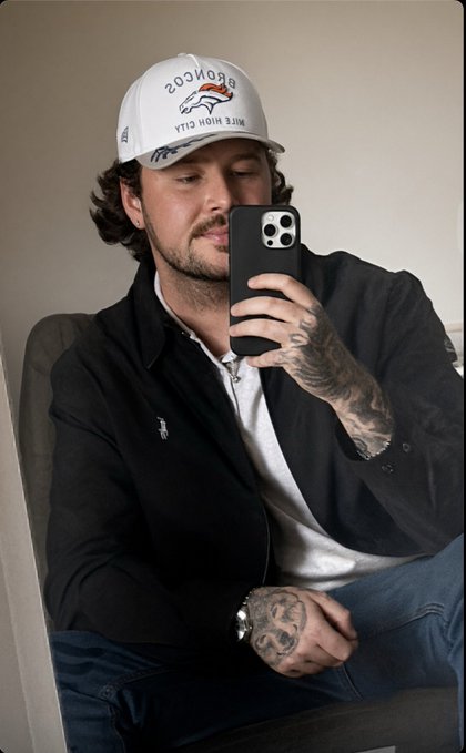 A man with curly hair and a mustache takes a mirror selfie while wearing a white Broncos "Side Action City" cap, a black jacket, and a white shirt, showing his tattooed hands holding a phone.

The casual, laid-back mirror selfie vibe fits perfectly with the "GM 🌤️ happy Wednesday" greeting, offering a relaxed morning check-in with fans.