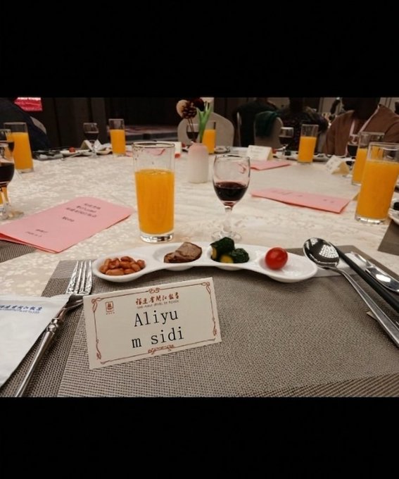 The image shows a dining table set up with various items, including plates of food, glasses filled with orange juice, and wine glasses. There are also some papers on the table that appear to be menus or instructions for the meal. A person is visible in the background, possibly attending to other tasks or waiting for their turn to enjoy the meal. The overall atmosphere seems to be one of anticipation and enjoyment as people gather around the table to share a meal together.