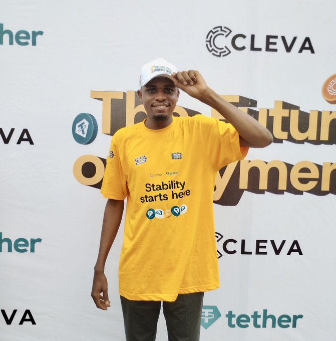 A young man wearing a cap and a yellow "Stability starts here" t-shirt poses confidently at a Cleva/Tether-sponsored event, celebrating his return to the web3 space after completing his degree. The branded backdrop reinforces his enthusiastic comeback message to the crypto community.