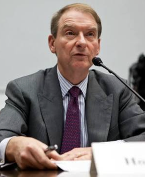 A man in a dark suit, striped shirt, and patterned tie speaks into a microphone at a hearing, with a nameplate partially visible reading "Wa..." (likely Paul Atkins, current SEC Chairman). The image relates to the SEC crypto task force memo as it likely depicts Atkins, who oversees the agency that met with the Hyperliquid Policy Center regarding DeFi regulatory discussions.