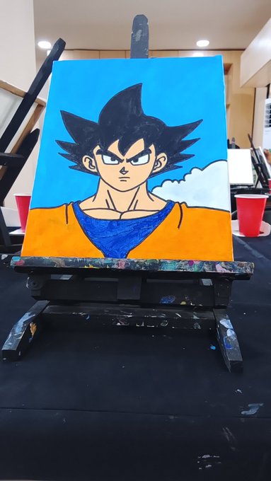A hand-painted canvas of the anime character Goku from Dragon Ball, displayed on an easel in what appears to be an art studio.
