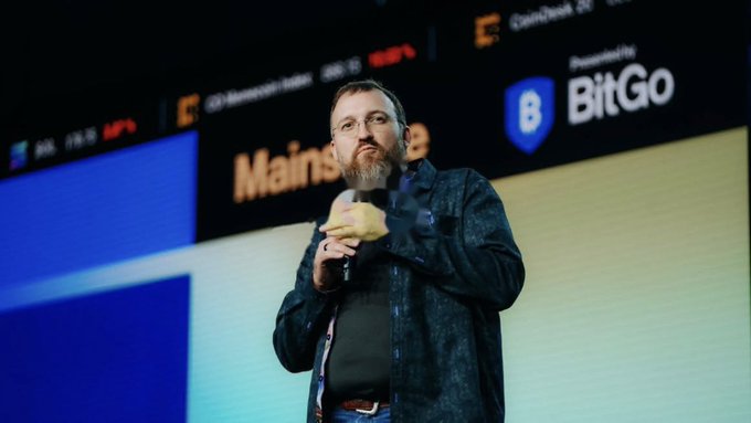 A man with a beard speaking into it while standing on a stage with a 'BitGo' logo and 'Mains' text visible in the background.