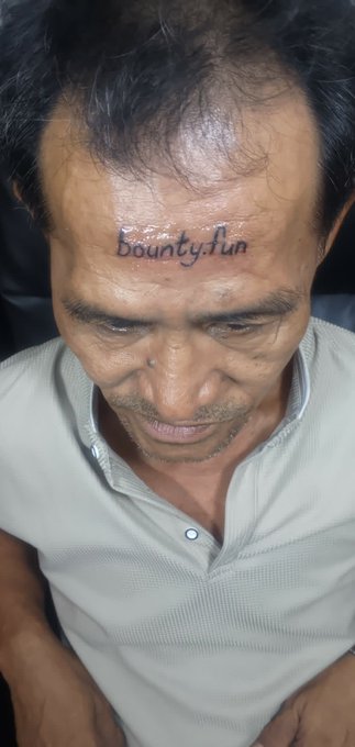The image shows a close-up view of a person's head, specifically their forehead, which has a tattoo of the word "bountyFun" written on it. The tattoo appears to be permanent and is located above the person's eyes. The photo also contains text that reads "Another man just cashed out 200 SOL (13,270) for a forehead tattoo. A young man from South Asia permanently tattooed his forehead with ". This suggests that the image might have been taken at an event or gathering where people are exchanging items of value, such as tattoos, and the person in focus is one of those individuals who has received a tattoo.