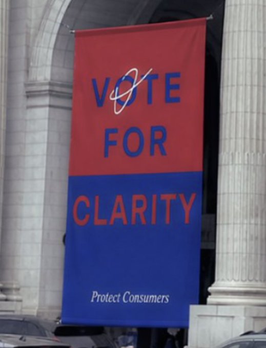 A red and blue banner hanging on a building reads 'VOTE FOR CLARITY' with 'Protect Consumers' at the bottom.