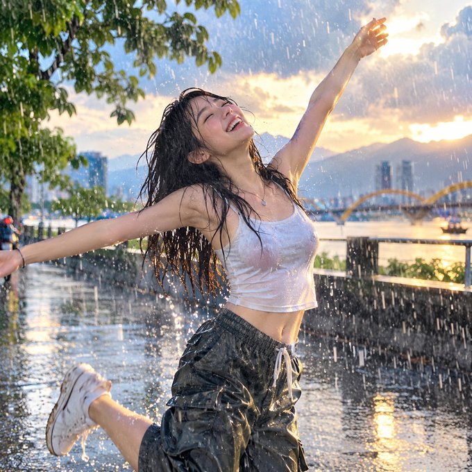 A young woman with long wet hair joyfully plays in the rain with her arms outstretched, set against a backdrop of a city skyline, bridge, and sunset.