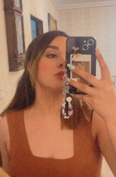 A mirror selfie of a woman with brown hair wearing a brown top and a jeweled phone charm.