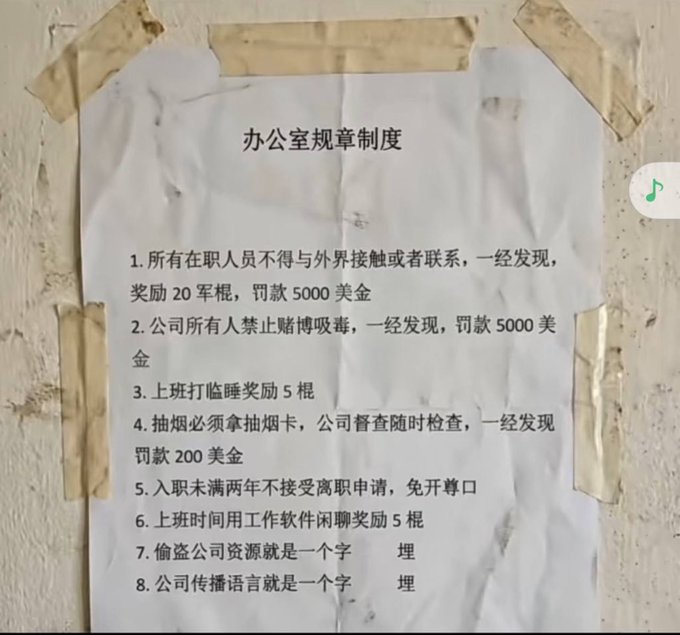 A handwritten Chinese sign titled "办公室规章制度" (Office Rules and Regulations) taped to a wall, listing eight rules including fines of 5000 USD for external contact or drug use, 200 USD fines for smoking without a card, and rewarding cigarettes for dozing off or chatting on work software.