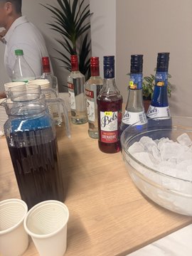 A beverage station at SuperteamSG features purple and blue drinks labeled with "Bols" and "Safari" brands, served alongside a bowl of ice, with a blue pitcher in the foreground.