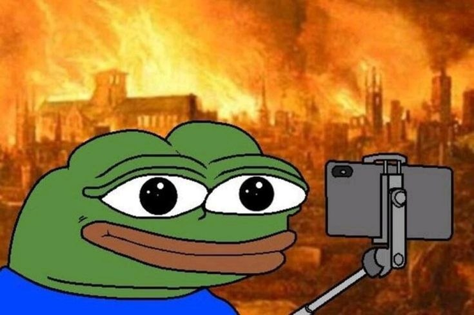 A Pepe the Frog meme character holding a smartphone on a selfie stick, taking a photo with a fiery, apocalyptic destroyed cityscape in the background.