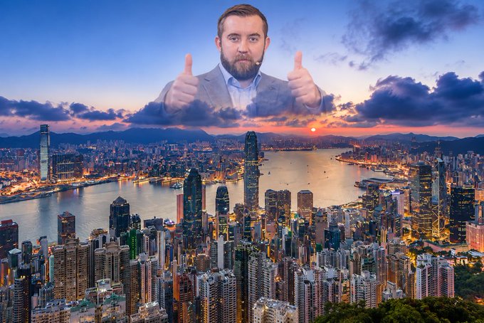 A man in a suit giving two thumbs up appears to float among the clouds above a panoramic view of Hong Kong's skyline at sunset, with Victoria Harbour visible below.