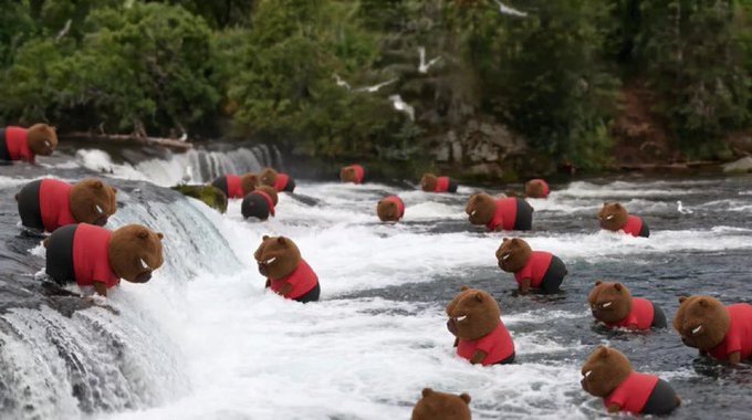Numerous brown figures wearing red and black clothing are positioned in a rushing river near a waterfall, with forested terrain in the background.