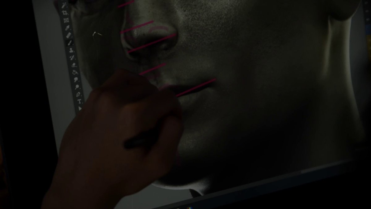 The image shows a person's hand holding a pen, drawing lines on a computer screen or monitor. The focus of the image is on the hand and its movement as it creates lines on the screen. There are no other objects present in the image, and there is no text visible. The primary subject matter appears to be related to graphic design or digital art, possibly involving the creation of a character or illustration.