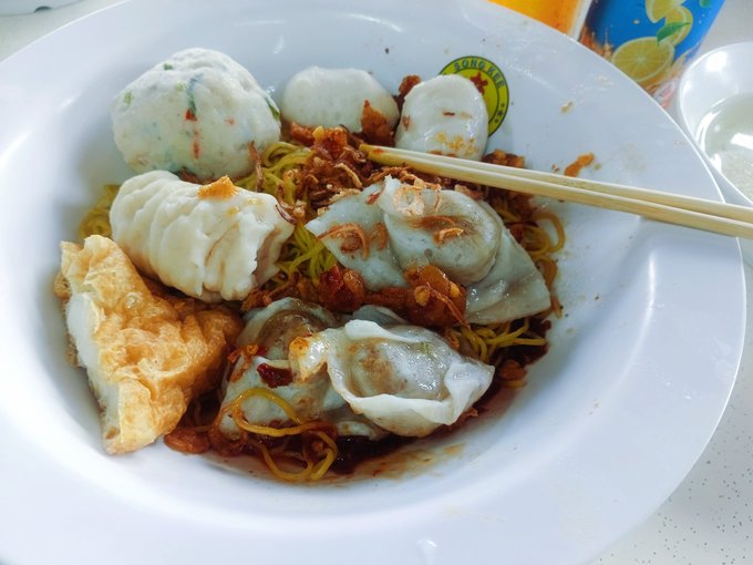 A plate of dim sum featuring dumplings, fried items, and noodles, with chopsticks resting on the side of the white bowl.