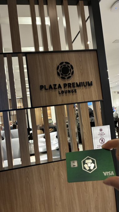 A person holds a green Visa card in front of the entrance to a 'Plaza Premium Lounge' featuring wooden slat design and a logo on the wall.