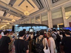 A crowded convention hall with attendees gathered around what appears to be a stage or display area.