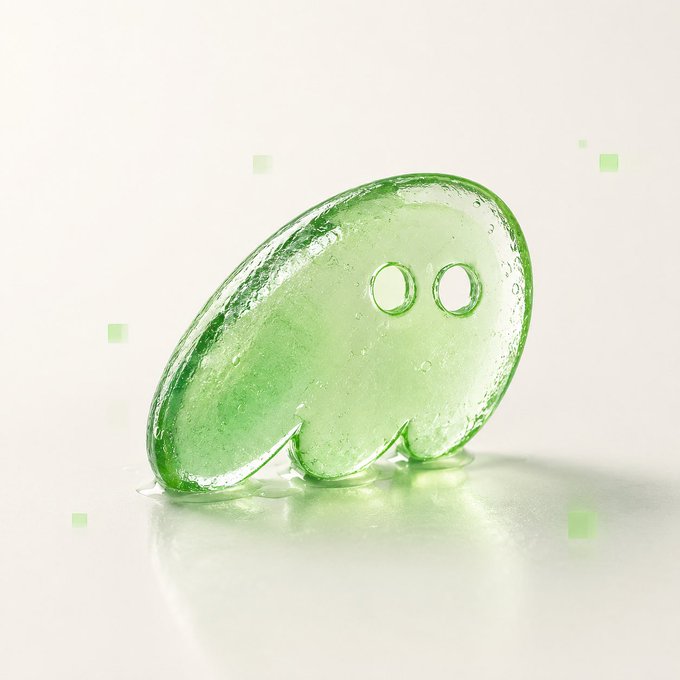 A glossy, translucent green ghost-like figure with two hollow eyes stands on a reflective surface, surrounded by small green squares floating in the air—its jellybean-shaped body and spectral appearance visually embodying the "phantom" referenced in the caption's message about renewed hope in green.