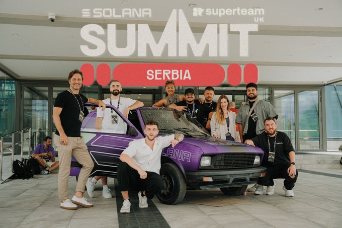A group of people posing around a purple car at the 'SOLANA SUMMIT SERBIA' event hosted by Superteam UK.