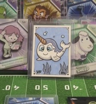 A VeeFriends trading card depicting a cartoon narwhal with a "VF" logo, displayed among other cards on a green field-patterned surface.