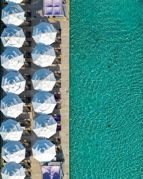Aerial view of a beach resort showing two rows of white umbrellas and sun loungers arranged neatly beside turquoise water.