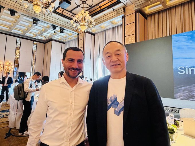 Two men pose together at an upscale event venue with ornate chandeliers and a screen displaying partial text "sin" in the background. The post identifies the man on the right as Dr. Xiao Feng, founder of HashKey, captured here following the launch of institutional Bitcoin staking with Stacks.