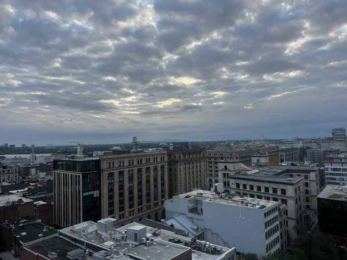 An aerial view of an urban cityscape at dawn or dusk with dramatic cloud cover over rooftops and buildings.
