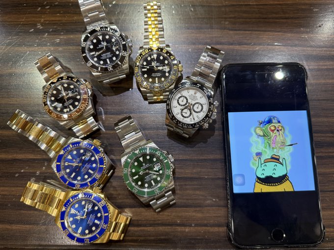 A collection of seven luxury-style watches arranged on a wooden table next to a smartphone displaying a cartoon character wallpaper.
