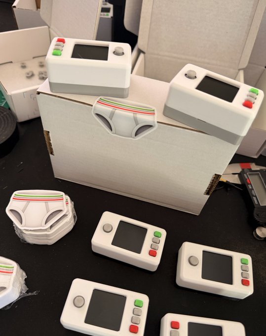 Several white handheld electronic devices with small screens and colored buttons sit on a black table alongside white VR headset components.