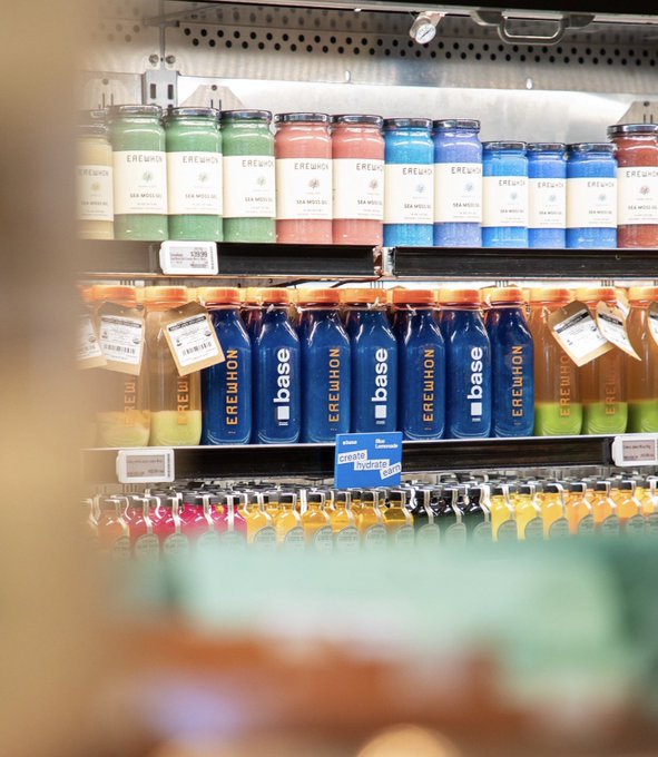 A refrigerated store shelf displaying rows of colorful Erewhon branded beverages including "Sea Moss" drinks in green, pink, and blue, along with "Base" brand electrolyte drinks in blue and orange varieties.