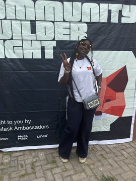 A person wearing a white shirt, dark pants, and a crossbody bag poses in front of a banner with text including 'COMMUNITY', 'Mask Ambassadors', and a Meta logo.