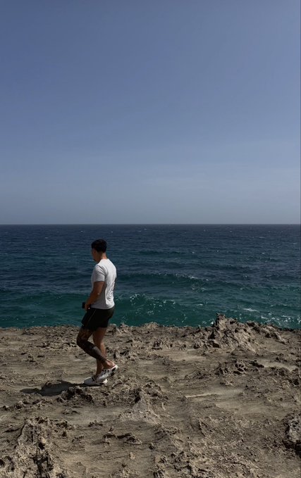 A man jogs along a rugged coastal cliff overlooking the expansive ocean under a clear blue sky, capturing a refreshing start to the morning that aligns with the upbeat "Gm" greeting.