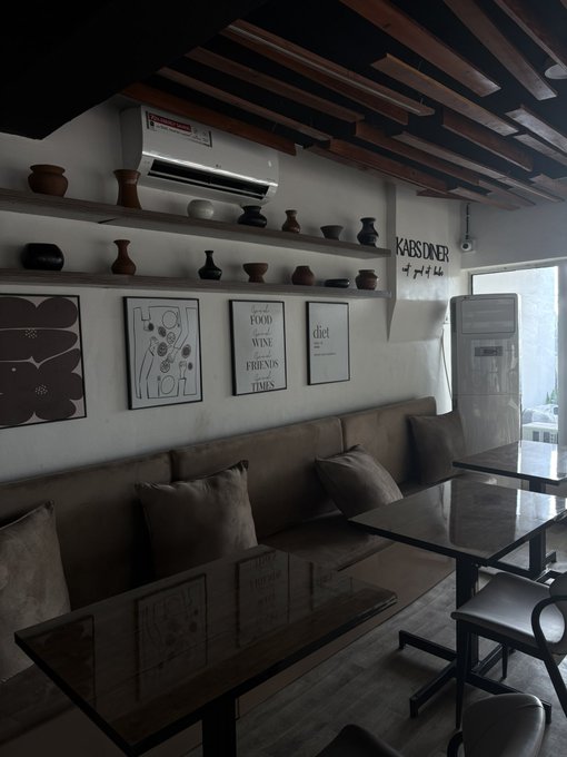 Interior of a cozy cafe or restaurant named 'KAISIDINER' featuring exposed wooden ceiling beams, shelves with pottery and vases, framed wall art with quotes like 'Good WINE Friends Times,' and booth seating with brown cushions.