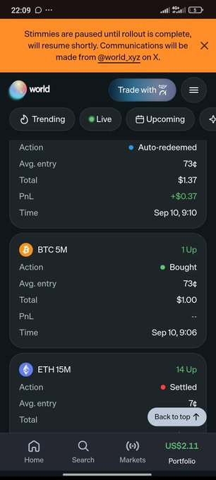 A mobile app screenshot showing a trading interface with sections for 'Action', 'BTC 5M', and 'ETH 15M', with a notification at the top stating 'Stimmies are paused until rollout is complete.'