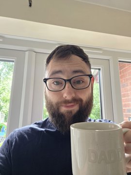 A bearded man with glasses smiles at the camera while holding a white "DADDY" mug, likely enjoying a morning coffee as he greets his followers with "Gm" and discusses his $IREN stock investment and upcoming holiday plans.