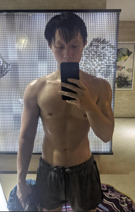 A man with a lean, muscular physique takes a shirtless mirror selfie, wearing only dark shorts and holding a smartphone to capture his reflection. The image humorously illustrates the post's joke about crypto founders' tendency to share shirtless selfies, suggesting this is a typical example of the trend being mocked.