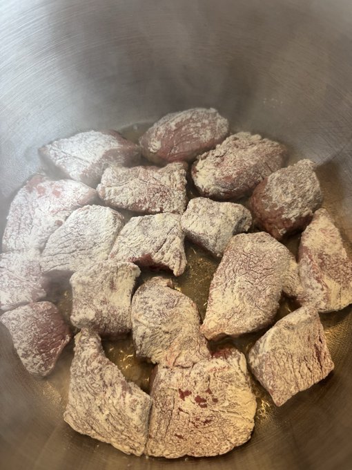 Raw chunks of meat coated in white powder are cooking in a metal bowl with visible steam rising from them.