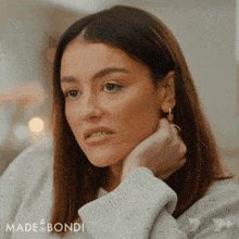 The image features a woman with long brown hair wearing a white sweater, looking down at her hand or chin while sitting indoors. The caption below the photo reads "made&bordi", which could be a brand name or possibly an artist's name.