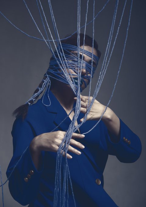 The image features a woman with her eyes closed, wearing a blue jacket over a black shirt. She has long hair tied up in a ponytail, and she's holding onto a bunch of strings that are wrapped around her head. The strings appear to be blue, adding an artistic touch to the scene. The post seems to be discussing the concept of "string" or "strings," possibly referring to the woman's hair or the strings themselves.