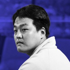 A black-and-white close-up portrait of an Asian man looking over his shoulder against a blurred dark blue background.