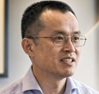 A smiling middle-aged man with glasses and short dark hair, wearing a light-colored shirt, is shown in a close-up portrait—the post's caption "Are you telling me this is CZ?" humorously suggests the resemblance to Changpeng Zhao, the Binance founder.