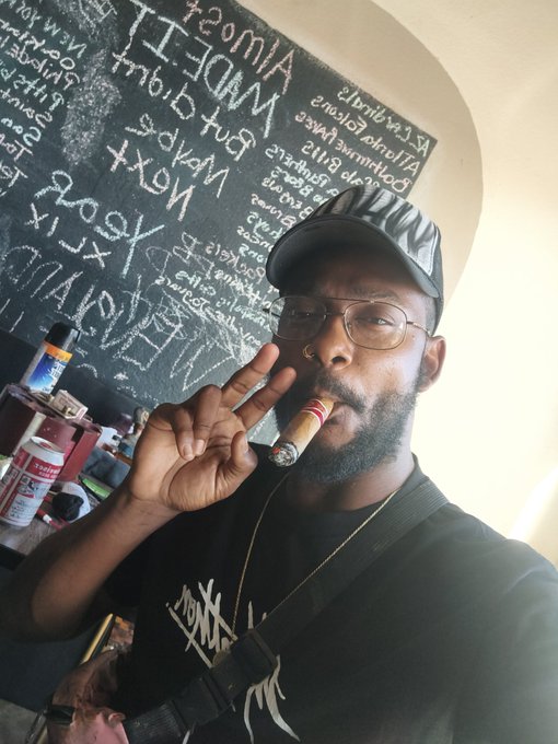 The image features a man wearing glasses, a black shirt, and holding a cigar up to his face while posing for a photo. The caption of the image reads "#Day545 #Apecoin A Supporting #APE A Selfie until ApeCoin hits a all-time high #yuga @apecoin Blessings ApE". This post seems to be promoting an app called Apecoin, which is likely related to the man's interests or lifestyle. The caption also mentions that the post was created by someone named "yuga" and includes a hashtag "#apecoin".